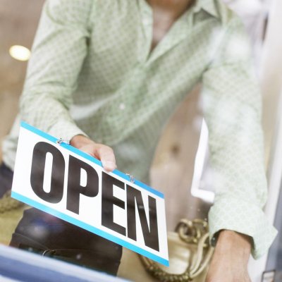 A man placing an "Open" sign indicating that his business is now open...for business