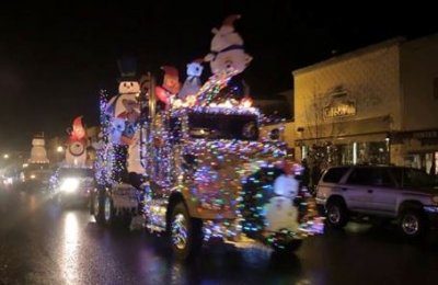 A semi-truck adorned with Christmas decorations leads a parade of similarly adorned trucks